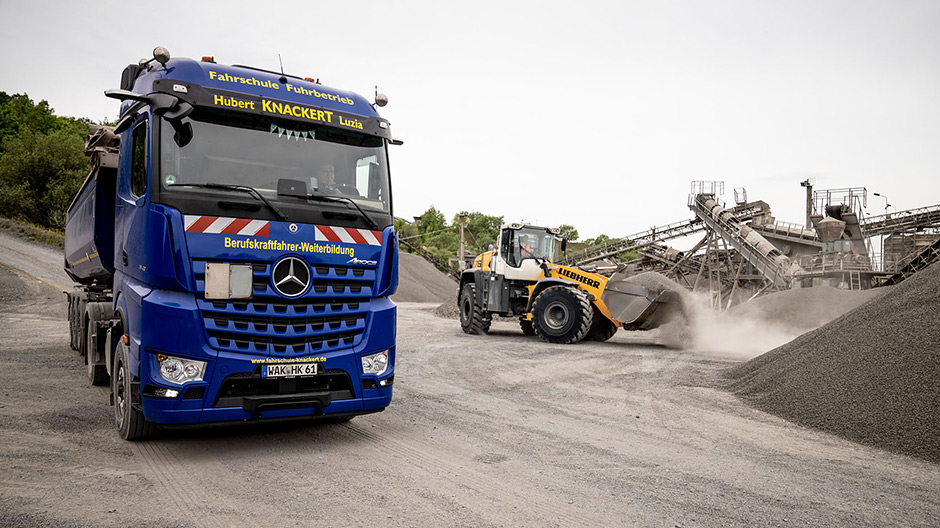 El camión articulado basculante Arocs carga material para la construcción vial en una cantera de basalto: grava, piedras y anticongelante de basalto.