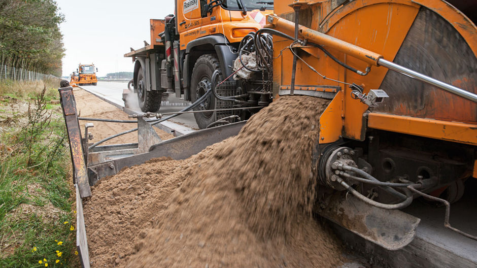 Procédé et quantités précis. L’U 500 laisse le matériau d’accotement s’écouler sur le bord de la route. Sur le chantier de l’A24, c’est un mélange préparé de gravier, de sable et de gravillons qui est utilisé.