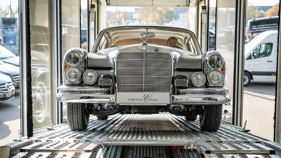 Raspaardje. Een Mercedes-Benz 300 SE/Coupé uit 1966 rijdt de oprijplaat van de gesloten autotransporter op.